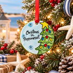 A flat, round ceramic ornament with a Christmas tree and the text 'Christmas in Popponesset' painted on it, packaged in a gift box.