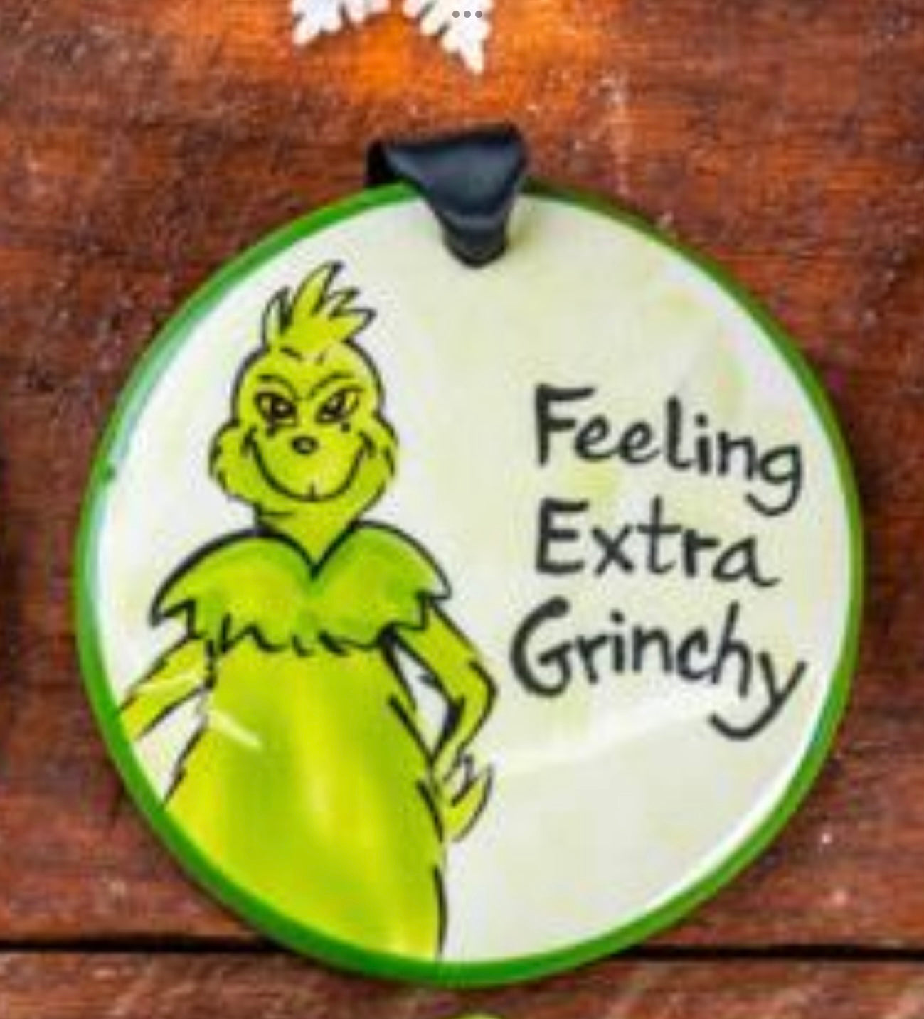 A round ceramic ornament with a hand-painted illustration of the Grinch and the text 'Feeling Extra Grinchy'.