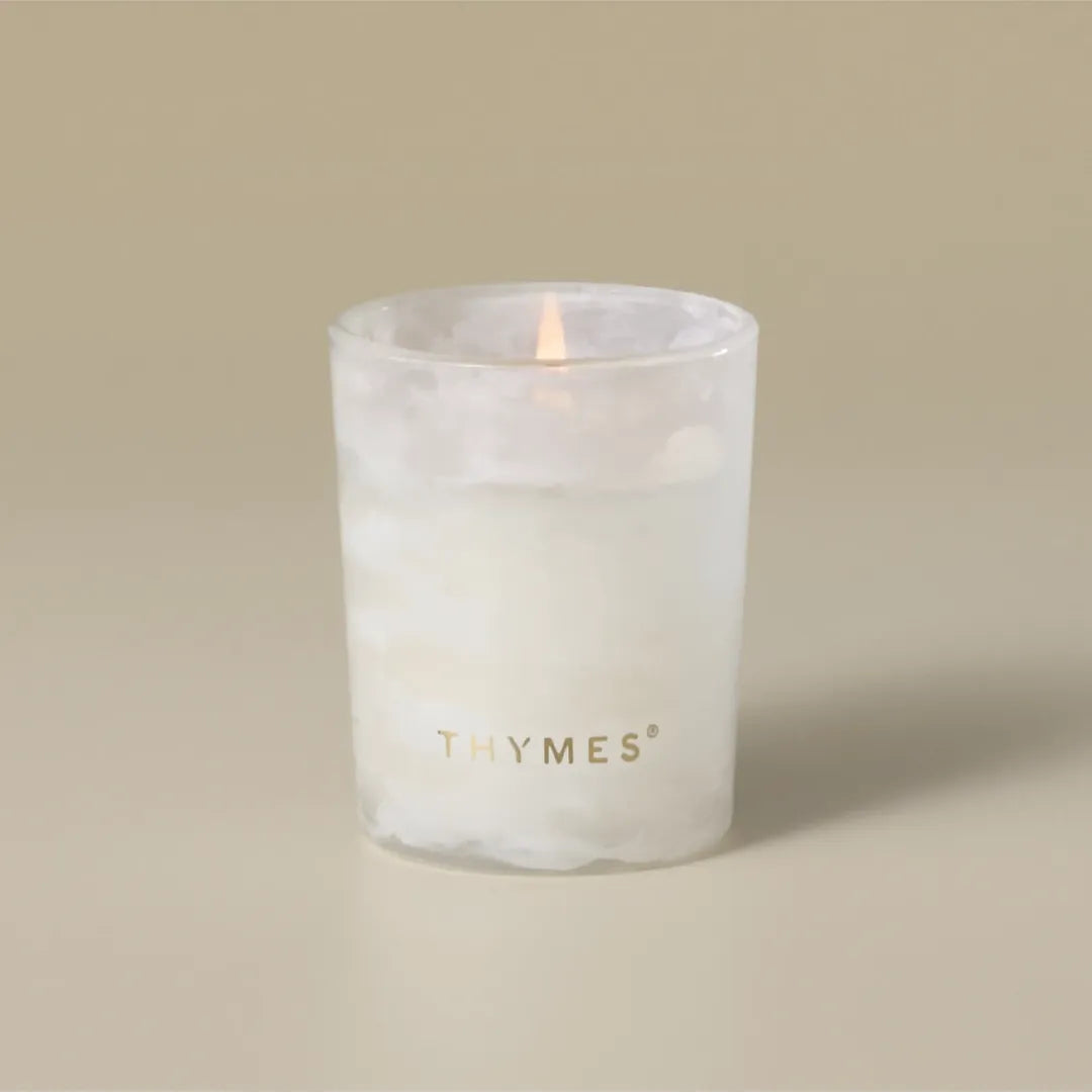 Thymes Frasier Fir Tidings 2 oz boxed votive candle in a swirling winter-white glass vessel with gold accents, displayed beside its green holiday gift box.