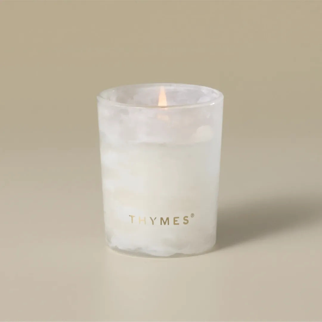Thymes Frasier Fir Tidings 2 oz boxed votive candle in a swirling winter-white glass vessel with gold accents, displayed beside its green holiday gift box.
