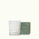 Thymes Frasier Fir Tidings 2 oz boxed votive candle in a swirling winter-white glass vessel with gold accents, displayed beside its green holiday gift box.