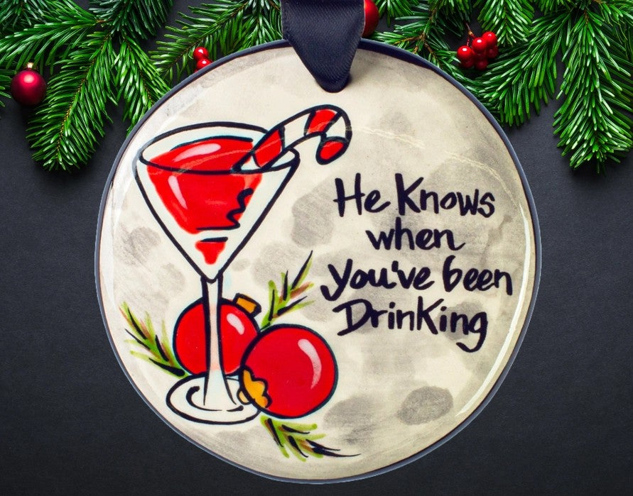 Hand-painted ceramic Christmas ornament featuring a red cocktail with candy cane garnish and the funny saying He Knows When You've Been Drinking, 3.5 inches.