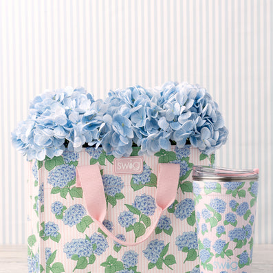 Swig Hydrangeas Reusable Gift Bag featuring clusters of soft blue hydrangeas on a blush and white pinstripe background
