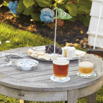 Outdoor setting with a wooden table, drinks, snacks, and a person pouring beer.