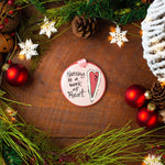 A round ceramic ornament with the text 'Nursing is a Work of Heart' painted on it, displayed among Christmas decorations on a wooden background. Hand painted  in USA