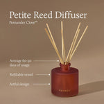 A reed diffuser bottle in a deep rose-red tone with natural reed sticks, shown on a warm beige background with text reading 'Petite Reed Diffuser' and 'Pomander Clove.' Callout lines mention average 60-90 days of usage, refillable vessel, and artful design.