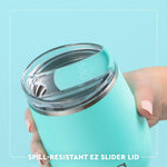 Turquoise tumbler with a spill-resistant EZ slider lid held by a hand against a light blue background.