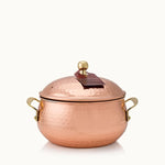 A hammered copper lidded pot with brass side handles and a small brass knob on the lid, shown on a plain light background.
