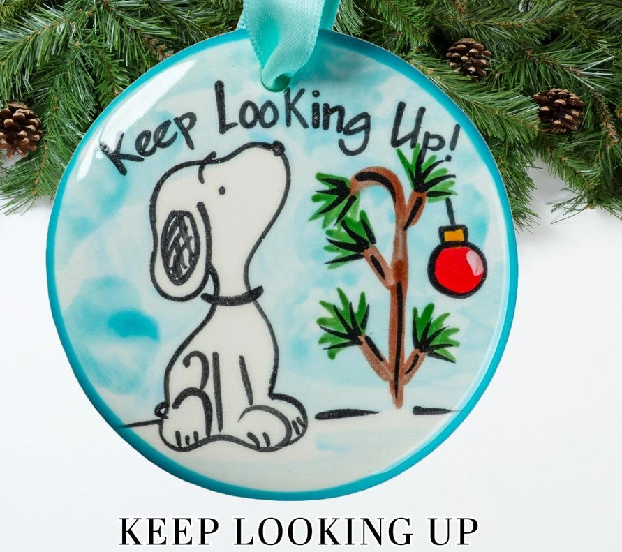 Hand-painted ceramic Keep Looking Up Christmas ornament featuring a white dog, evergreen branch, and red holiday ornament on a turquoise background.
